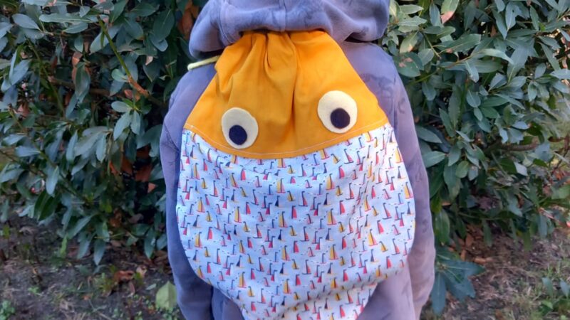 Enfant de dos portant un sac poisson fait main sur le dos